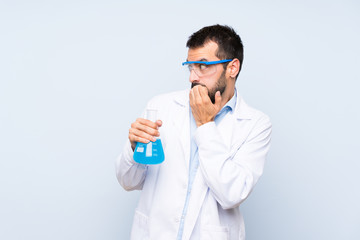 Young scientific holding laboratory flask over isolated background nervous and scared putting hands to mouth