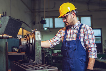 Turner worker is working on a lathe machine in a factory.  