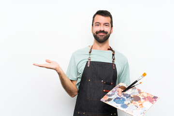Young artist man holding a palette over isolated background holding copyspace imaginary on the palm...