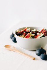 a bowl of healthy Breakfast with oatmeal, figs and cashew nuts on a white table with a bamboo spoon. vegan food