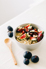 a bowl of healthy Breakfast with oatmeal, figs and cashew nuts on a white table with a bamboo spoon. vegan food