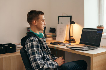 Teenage boy doing homework using computer sitting by desk in room alone