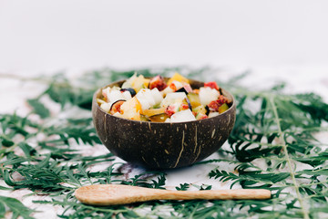 healthy fruit salad in a plate of coconut shells on the table with tropical leaves. vegetarian food