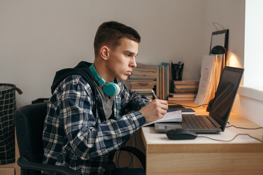 Teenage boy doing homework using computer sitting by desk in room alone