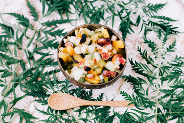 healthy fruit salad in a plate of coconut shells on the table with tropical leaves. vegetarian food
