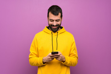Handsome man with yellow sweatshirt sending a message with the mobile