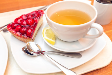 Closeup of a teacup with lemon tea and a piece of raspberry cake.