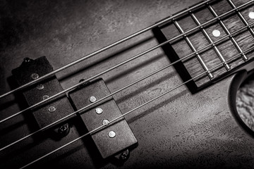 Bass guitar with four strings in black and white closeup. Detail of popular rock musical instrument. Vintage style photo of bass guitar pickups and neck.