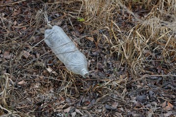 a large dirty white plastic bottle lies on gray dry grass and fallen leaves on nature