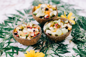 healthy fruit salad in a bowl of coconut shells on the table with tropical leaves. vegetarian food