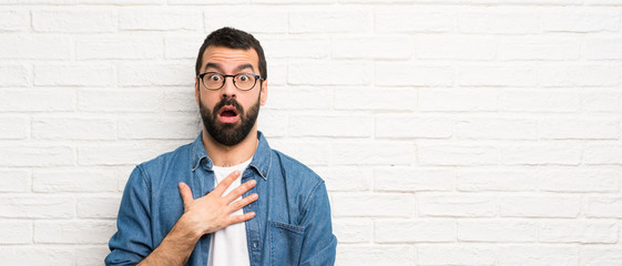 Handsome man with beard over white brick wall surprised and shocked while looking right
