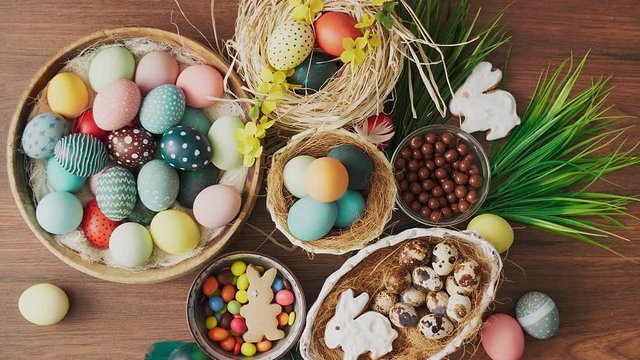 Feathers falling on colorful Easter eggs in nest and spring flowers on wooden table. Easter holiday decorations, Easter concept background.
