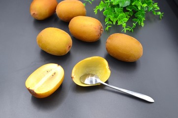 Golden kiwi and stainless steel spoon on black background