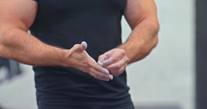 Athlete puts chalk on his hands before training. Chalk flies with hands. Close-up.