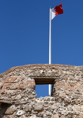 Flagge von Bahrain auf dem Arad Fort im Wind vor strahlend blauem Himmel