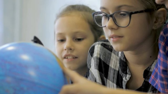 Geography lesson. Schoolmates are studying the globe on the background of a school board