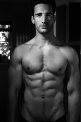 Fototapeta na wymiar Handsome shirtless man with beard and sixpack abs standing in doorway with unbuttoned jeans