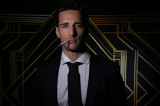 Portrait of handsome man in suit and tie in front of art deco backdrop with cigarette hanging from his lips