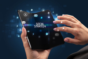 Businessman holding a foldable smartphone with SOCIAL STRATEGY inscription, social networking concept