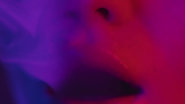 Sexy model lips in colorful neon light exhaling smoke of electronic cigarette or vape. Smoking girl, lips close-up, ultraviolet pink and blue light. Sexy woman smoking. Woman mouth closeup, slowmotion
