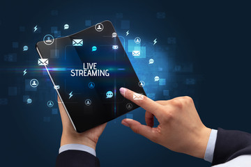 Businessman holding a foldable smartphone with LIVE STREAMING inscription, social networking concept