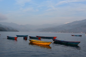 Fototapeta na wymiar yellow boat the others colour in mountain ranges background with fog and blue sky .phewa lake nepal
