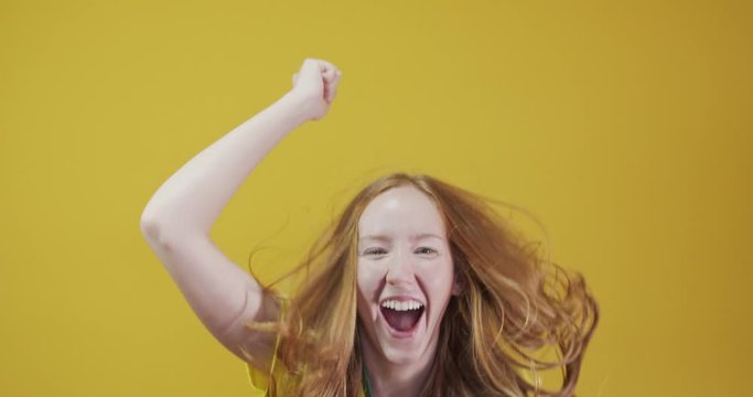 Brazil supporter. Brazilian redhead woman fan celebrating on soccer, football match on yellow background. Brazil colors. Wearing a t-shirt, flag and fan hat. 4K.