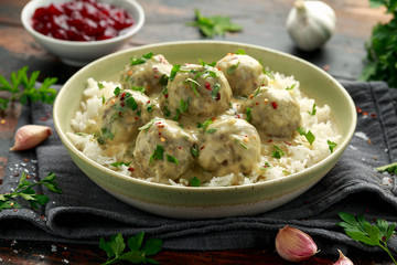 Hot Swedish meatballs with white rice and cranberry sauce on wooden table
