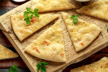 Fresh slices of Garlic pizza on wooden board with herbs.