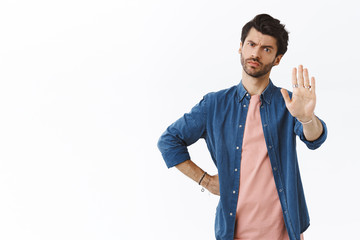 Judgemental and displeased, serious-looking handsome bearded man, grimacing from disapproval, dont permit something, raise arm in stop, never, prohibition gesture, standing white background