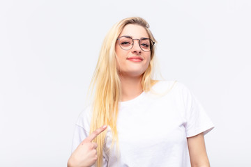 young pretty blonde woman looking proud, confident and happy, smiling and pointing to self or...