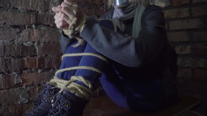 woman trying to free her hands from the rope. Sits in the basement, Close-up.