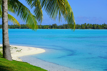 View of a tropical landscape with palm trees, white sand and the turquoise lagoon water in Bora...