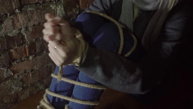 woman trying to free her hands from the rope. Sits in the basement, Close-up.