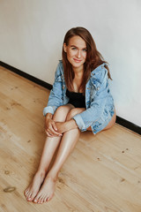Portrait of a cute girl with a luxurious figure sitting on the floor in a stylish denim jacket. Young mother in the last month of pregnancy