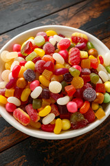 A mix of colorful candy in white bowl on wooden table