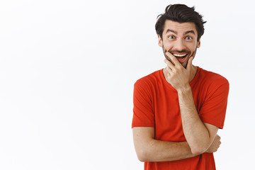 Waist-up portrait joyful enthusiastic young bearded man in red t-shirt, laughing and touching...