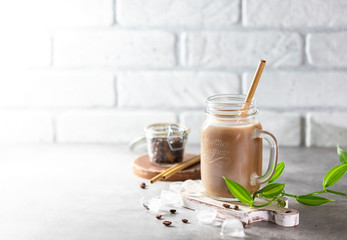 Ice coffee with milk and ice in a glass jar on a light background. Bamboo drinking straws with Zero - waste. Glass mason jar.