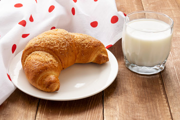 Croissant and a glass of milk on a wooden table.