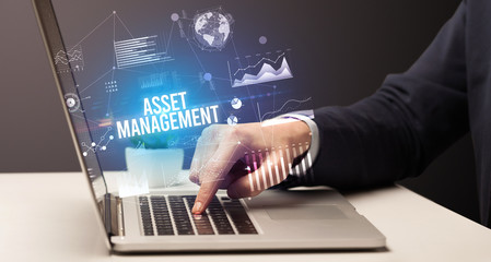 Businessman working on laptop with ASSET MANAGEMENT inscription, new business concept