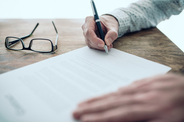 close-up of businessman signing contract or document at rustic wooden table