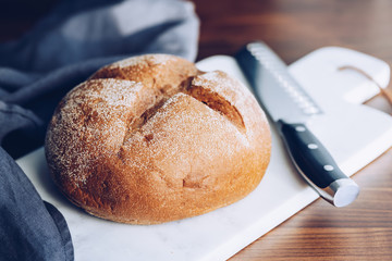 Rye bread loaf and a knife on a white marble cutting board.