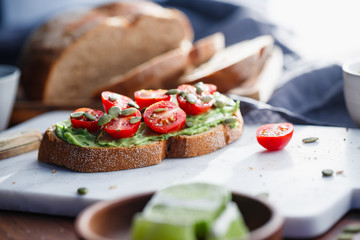 Avocado toast with cherry tomatoes and pepitas on a white marble cutting board. Home cooking, healthy eating concept.