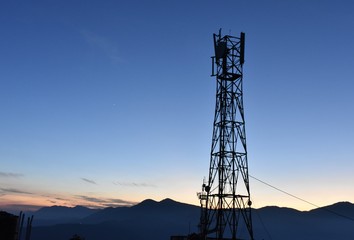 silhouette telecomunication tower on the mountains range and blue sky in sunset