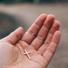 Eine Hand die ein goldenes Kreuz behutsam hält. Symbolisiert Vertrauen in Gott, Glaube, Kruzifix,...