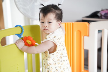 Portrait a cute girl 8 months baby standing and look at something outside the children partition...