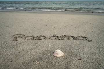 Fototapeta na wymiar Schriftzug Panama in den Sand geschrieben, mit einer Muschel, dem Meer und Horizont im Hintergrund, Urlaubsgrüße