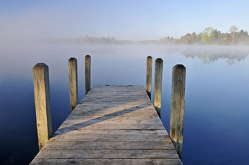 Naklejka premium Landscape of dock and foggy, spring shoreline of Whitford Lake, Fort Custer State Park, Michigan, USA