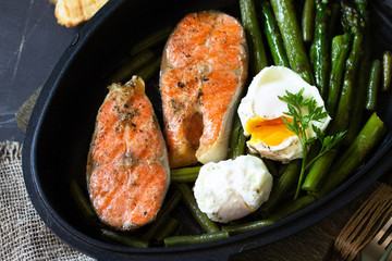 Green asparagus, grilled salmon and poached eggs. Healthy food on rustic wooden background.