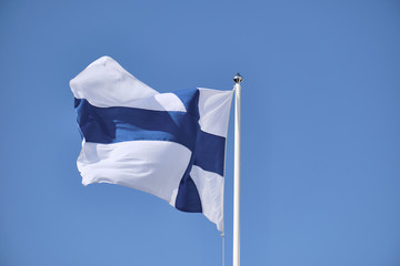 Flag of Finland on a white flagpole against a blue sky.